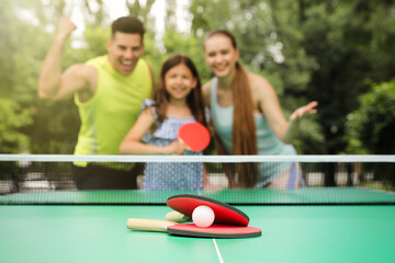 Wall Mural - Family near ping pong table in park, focus on rackets and ball