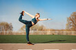 © Natalia - Woman is stretching her back and leg, standing in the lord of the dance pose outdoors at the stadium