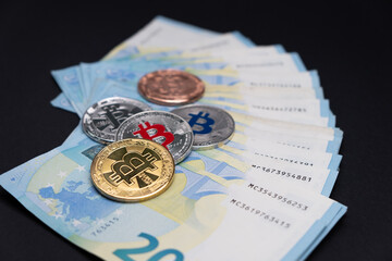 Bitcoins of various colours on top of 20 Euros bank notes. Bitcoins on twenty euros banknotes on dark background. Cryptocurrency concept, bitcoin and Euro banknotes. Cryptocurrency lies on money.