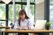 © saltdium - Asian businesswoman working at office desk with documents and laptop.