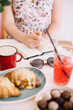 © anastasianess - Woman making notes in her notebook, while sitting by the cafe table, drinking coffee, enjoying summer strawberry lemonade, chocolate candy and croissants, with sunglasses and a flower vase standing