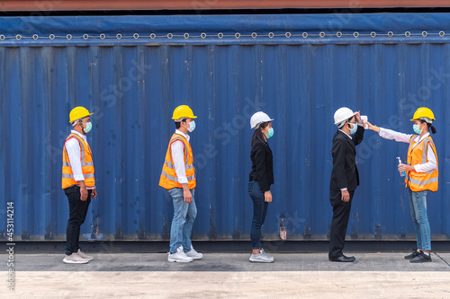 Factory workers wear face mask and safety dress measure body temperature and cleaning hand with alcohol sanitizer gel at outdoor warehouse - safety and health  protect coronavirus protocol concept