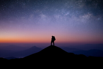 Wall Mural - Silhouette of young man traveler with backpack standing and watched the star and milky way alone on top of the mountain. He enjoyed traveling and was successful when he reached the summit.