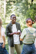 © LIGHTFIELD STUDIOS - Positive african ameican teenager holding smartphone near friends on blurred foreground
