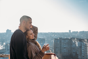 Young couple drinking coffee on the balcony of the apartment in the morning. Young happy couple, newlyweds family start new day and have morning coffee together