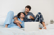 © LIGHTFIELD STUDIOS - blurred and happy gay couple looking at each other near laptop in bed