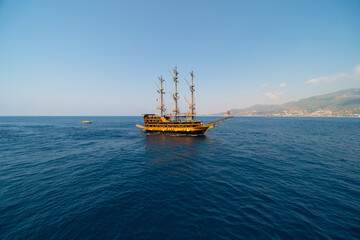 Wall Mural - Old pirate ship on the water of Mediteranean sea. Tourist entertainment, coastal tour. Summer sunny day. Mountain shore of Alanya. Turkey.