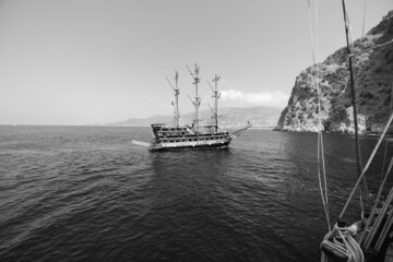 Wall Mural - Old pirate ship on the water of Mediteranean sea. Tourist entertainment, coastal tour. Summer sunny day. Mountain shore of Alanya. Turkey. Black and white