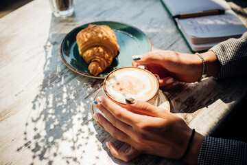 Cappuccino and croissant on the table in the cafe. The morning sunlight falls on the table, beautiful shadows appear.