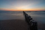 Fototapeta Morze - long exposure of an ocean sunset with sandy beach and wooden pylon storm groin in the foreground