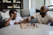 © Creative Flame - African American Father and son playing chess in living room