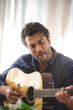 © chokniti - Handsome young man relaxing and enjoying playing guitar with eyes closed at home while feeling every rhythm