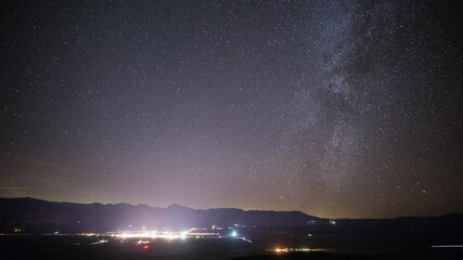 Wall Mural - beautiful time lapse of the stars moving across the night sky. the lights of a small town can be see