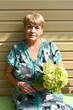 Portrait of 70 y.o. woman sitting on a bench and holding bouquet of hydrangea