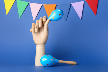 Wooden hand with Mexican maracas and garland on color background