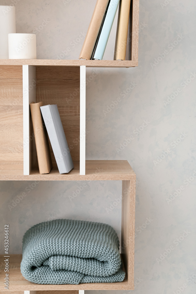 Book shelf with knitted plaid near light wall
