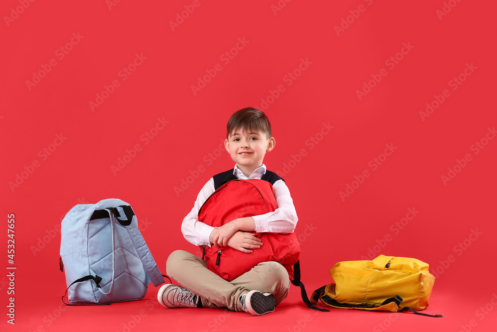 Little schoolboy with backpacks on color background