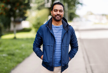 people, male fashion and leisure concept - portrait of happy smiling indian man in hooded jacket on city street