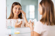 © Syda Productions - beauty, hygiene and people concept - teenage girl applying moisturizing cream looking in mirror at bathroom