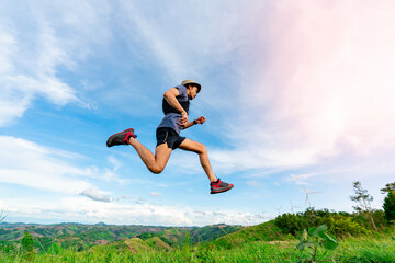 Asian man trail runners, wearing sportswear, are practicing running and jumping on the high mountain behind a beautiful view. There is a field of wind turbines generating electricity in the background