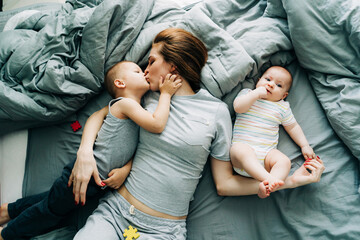 Happy moments of motherhood, mom with children on the bed embraces and kisses. Gentle family hug.