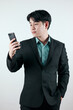 © Midnight Studio - Portrait of a handsome Asian man in a black suit holding a smartphone on white background. Concept of young businessman. with free space to copy