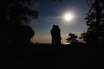 Couple at night standing in an embrace on the background of the full moon