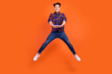 Poster - Photo of cute funky teen boy wear plaid outfit spectacles smiling jumping high isolated orange color background