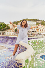 Wall Mural - Young cheerful woman sits with ice cream on a colored wall with arms open