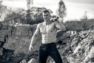 Strong shirtless bodybuilder training outdoor. Muscular handsome man posing outside.