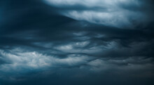 Photograph Of A Dramatic Isolated Asperitas Cumulus Thunderstorm Cloud As It Swirls And Moves Across The Sky Bringing Rain With Dark Blue Textures And Undulating Ripples And Waves Of Light.