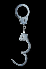 real zinc plated steel police handcuffs half-opened hanging vertically, isolated on black background