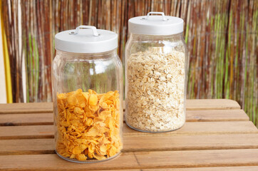 Closeup of two jars with oat-flakes and cornflakes on the wooden table