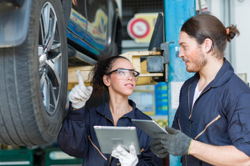 Wall Mural - Male and female car mechanic worker checking, repair and maintenance wheel at auto repair shop. Group of  mechanic vehicle service maintenance examining wheel tire at garage. Auto car repair service