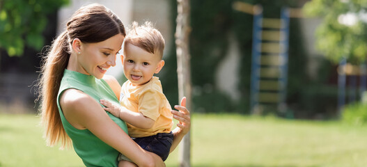 cheerful and young mother holding in arms toddler son sticking out tongue, banner