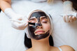 © руслан малыш - cosmetologist applying black mask on pretty woman face wearing black gloves, gorgeous woman in spa having facial procedures