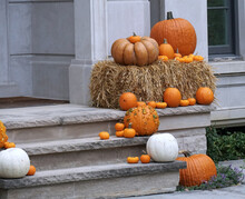 Front Steps Of Home With Different Sized Pumpkins And Straw As Halloween Decorations