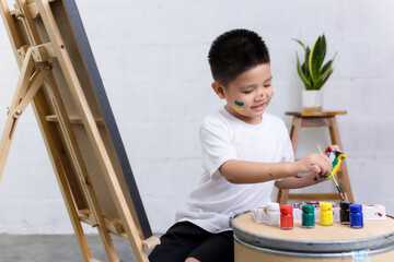 Cute happy little Asian boy painting with watercolor on canvas standing in white room at home, creative young artist at work. Kids paint. Children draw.