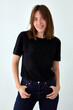 Positive female model wearing black t shirt and jeans standing with hands on waist against white background and looking at camera