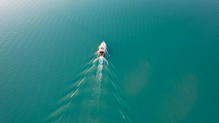 A white boat sails on Lake Balkhash at sunset. A beautiful long train on the water from the motor. The sky gradient is from orange to blue. Smooth water. Travel on a speed bot. Bertys Bay. Kazakhstan