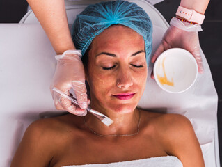 Adult woman receiving a beauty treatment with vitamins and gold cream on her face