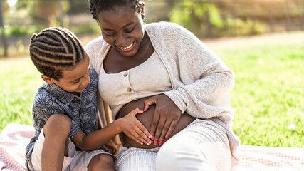 Happy African family expecting other baby - Afro Mother and son touching pregnant belly doing heart shape with hands - Parents love and maternity lifestyle concept