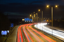 Smart Motorway In England, UK With Light Trails Signifying Busy Traffic At Rush Hour. The Banner Symbols Under The Gantry Sign Signify An End To Speed Restrictions.