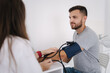 © Aleksandr - Young man with high blood pressure. Female doctor using sphygmomanometer with stethoscope checking blood pressure to a patient in clinic. Medical exam