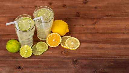 Two refreshing glasses of cold fruit juice with straw, ice lime and lemon juice, decorating with fresh lime and lemon on wooden table. Concept for refreshing