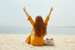 © PinkCoffee Studio - Woman with a long red hair sitting on the beach with raises hands. Happiness concept