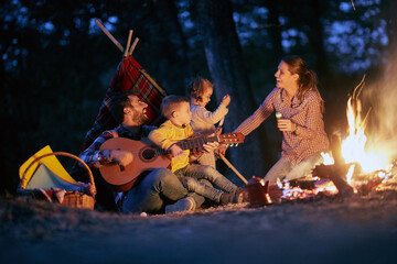 Wall Mural - A young happy family having a good time around a campfire in the forest