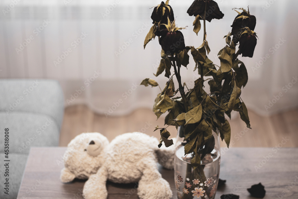 Flowers withered like love. Bouquet of red roses. In the background, a teddy bear on the table - obrazy, fototapety, plakaty 
