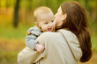 © MNStudio - Cute little baby boy in his mothers arms. Mom and son having fun on sunny autumn day in city park. Son being held by his mommy.
