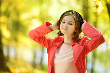 Wall Mural - Adorable young girl having fun on beautiful autumn day. Happy child playing in autumn park. Kid gathering yellow fall foliage.